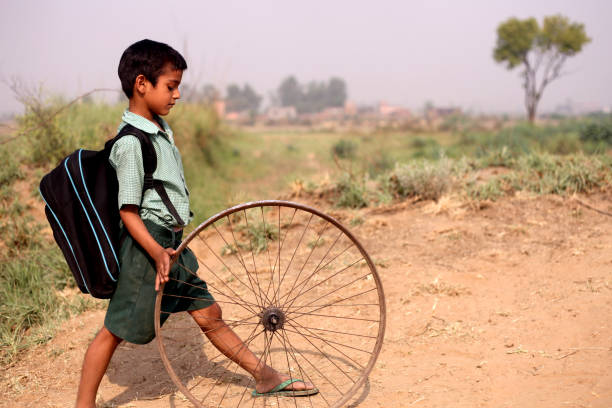 Poor child of Indian ethnicity running bicycle Tyre on country road.